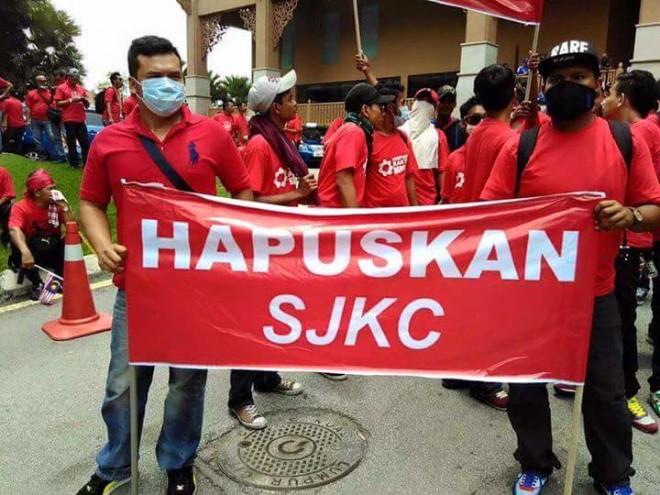 916集会现场的红衣人高举一面红色横幅，写着“消灭华小” - "Hapuskan SJKC"。