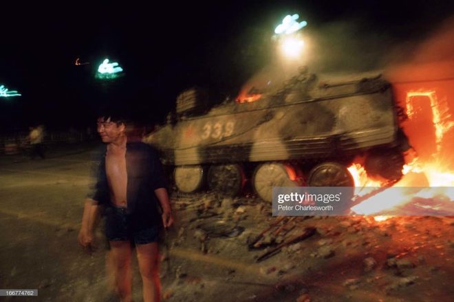 BEIJING, CHINA - 1989/06/04: A pro-democracy demonstrator passes a burning armoured personnel carrier (APC) during the fighting that raged on Changan Avenue as soldiers marched and shot their way towards Tiananmen Square on the night of the Communist Government's bloody crackdown on students and protestors.. (Photo by Peter Charlesworth/LightRocket via Getty Images)